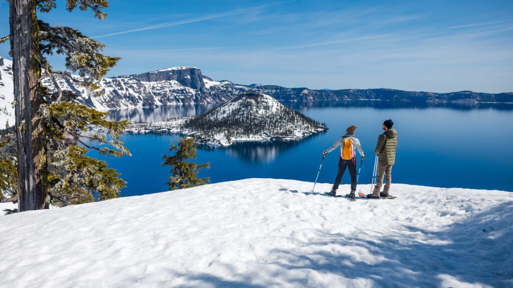 Two people stand on the edge above a blue lake.
